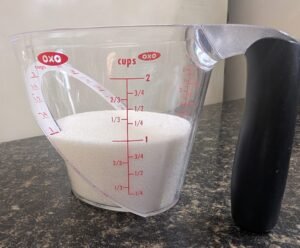 Measuring organic cane sugar in a glass cup for kombucha brewing